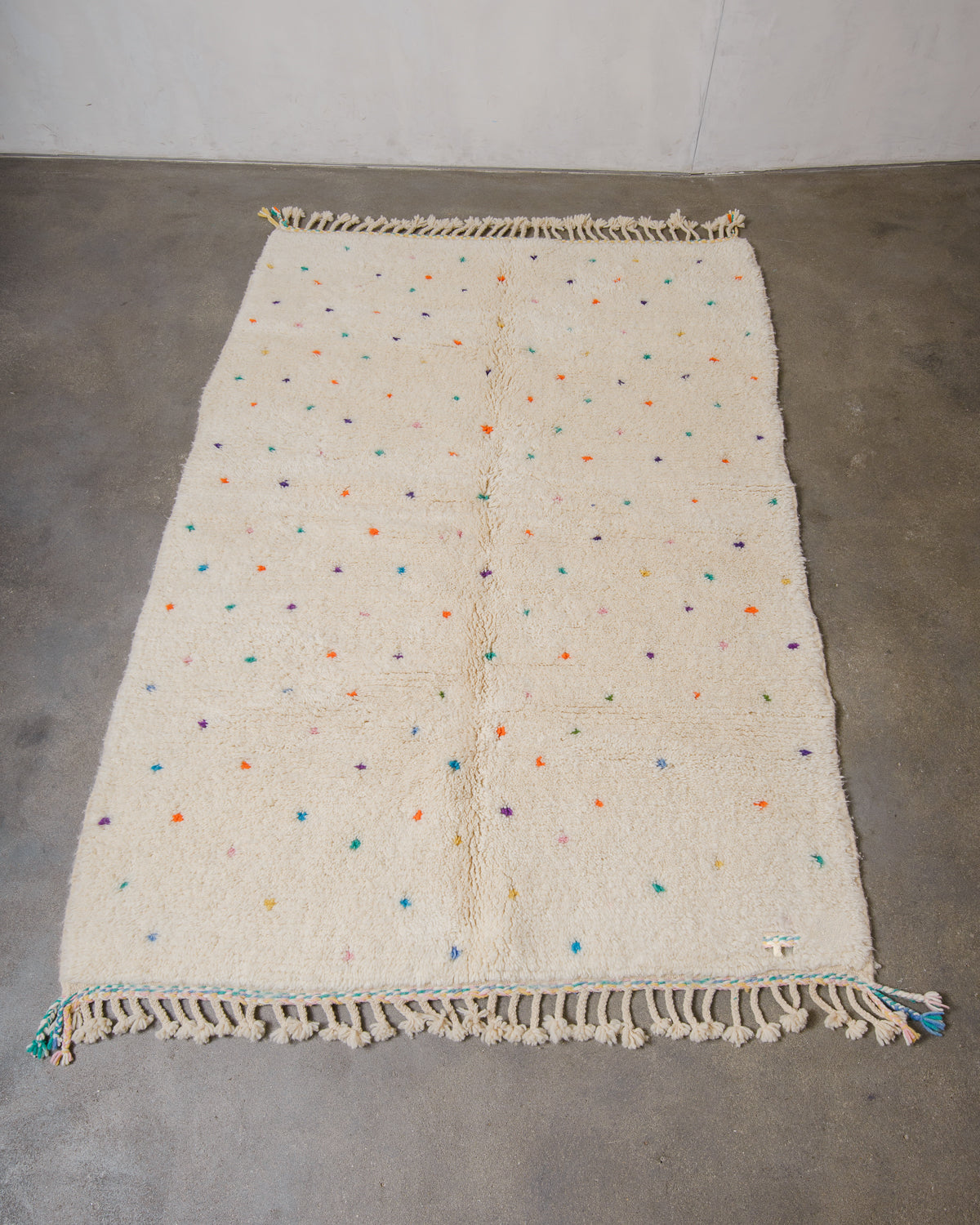 Berberlin Beniourain rug in cream wool with coloured dots laying on concrete floor.